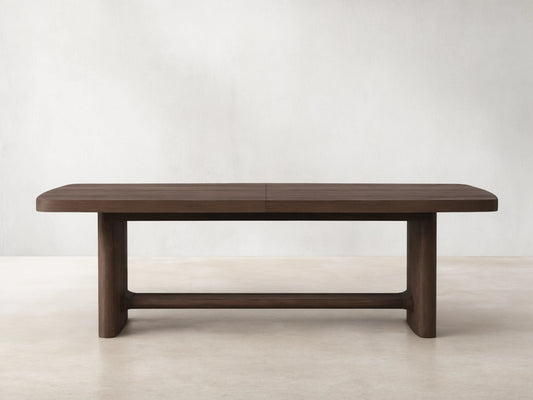 Front view of a dark brown wooden dining table with rounded corners, a central seam, and thick block legs connected by a stretcher.