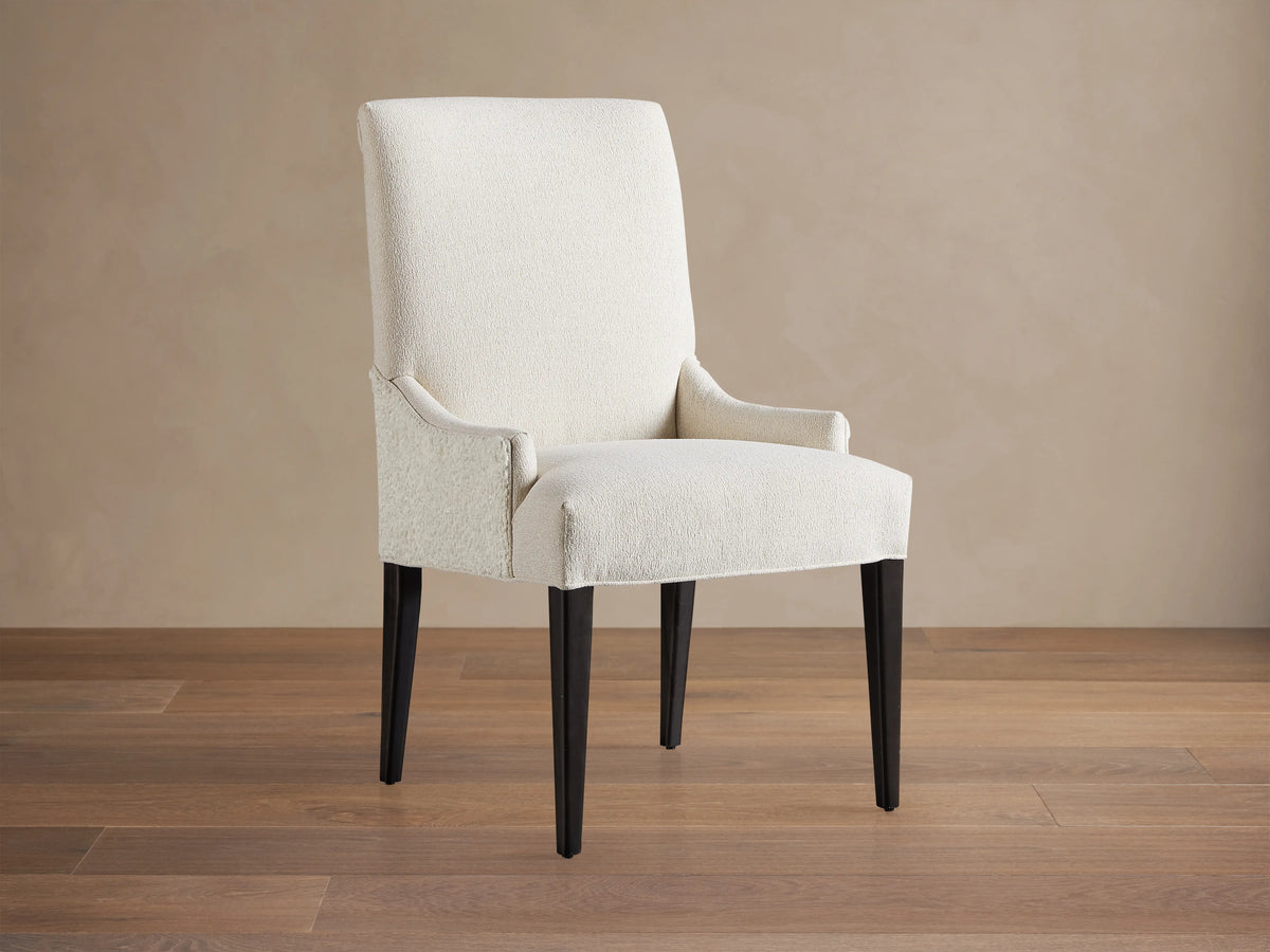 Rhen Dining Chair in off-white fabric with high backrest, slender tapering black legs, and slight armrest curves on wooden floor.