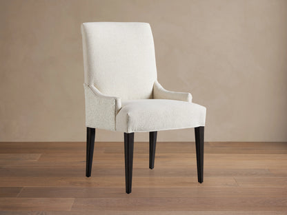 Rhen Dining Chair in off-white fabric with high backrest, slender tapering black legs, and slight armrest curves on wooden floor.