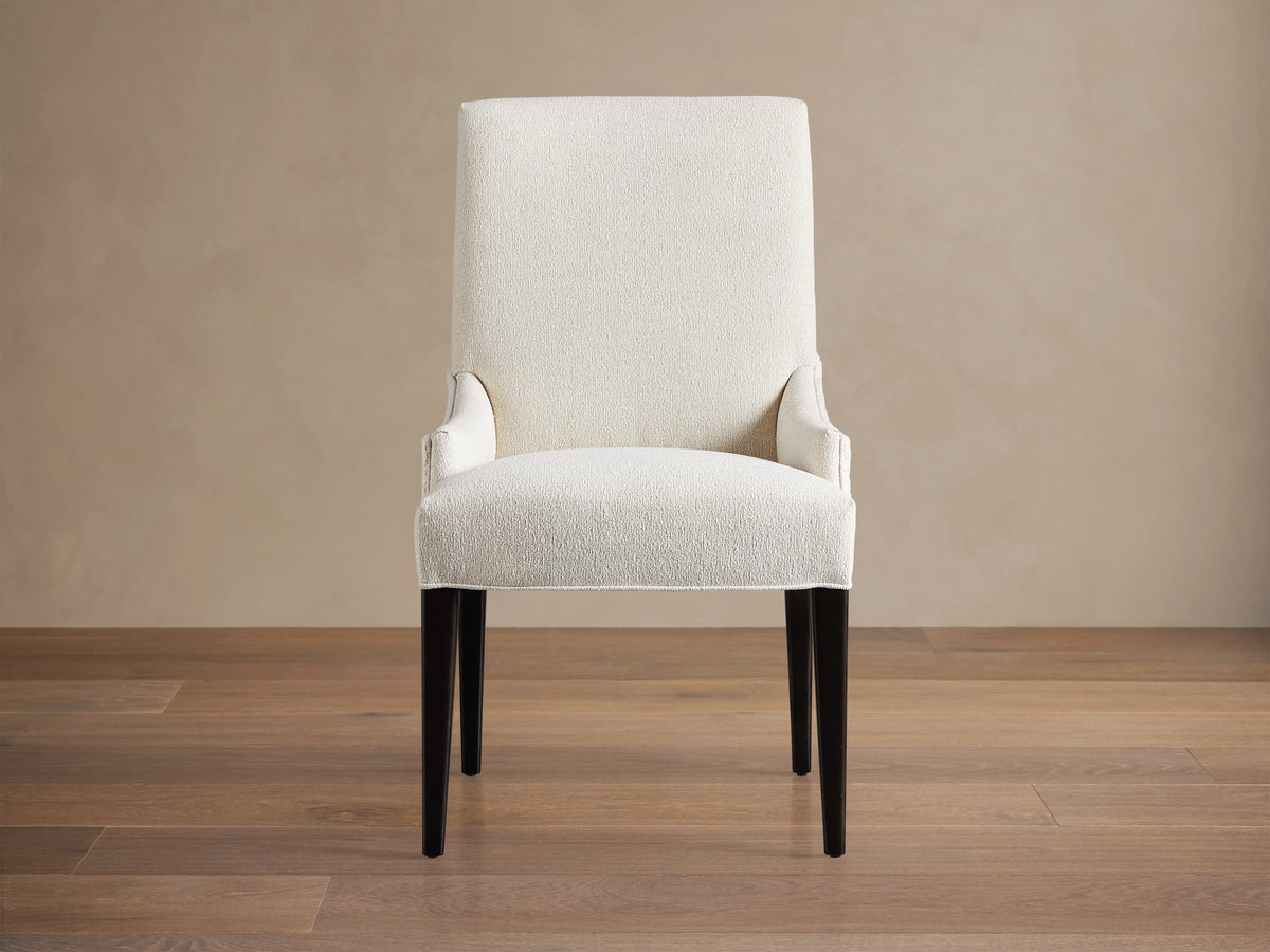 Rhen Dining Chair in off-white fabric with high backrest, slender tapering black legs, and slight armrest curves on wooden floor.