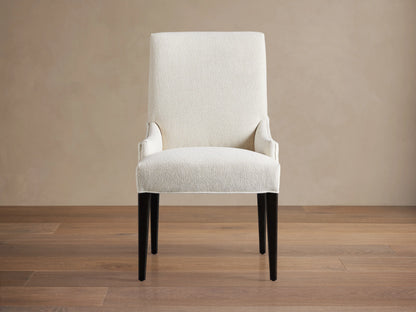 Rhen Dining Chair in off-white fabric with high backrest, slender tapering black legs, and slight armrest curves on wooden floor.