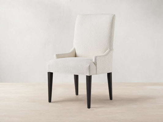 Rhen Dining Chair in off-white fabric with high backrest, slender tapering black legs, and slight armrest curves on wooden floor.