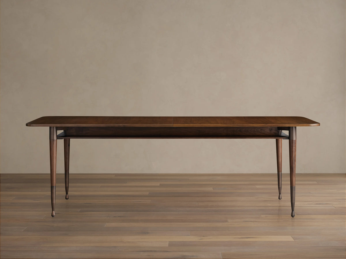 Ross Extension Dining Table made from walnut wood, featuring a long rectangular tabletop with patina brass leg caps and slender legs.