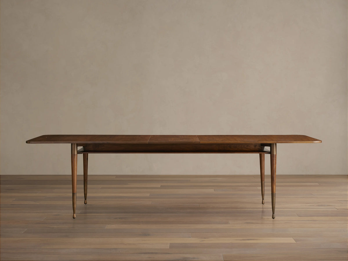 Ross Extension Dining Table made from walnut wood, featuring a long rectangular tabletop with patina brass leg caps and slender legs.