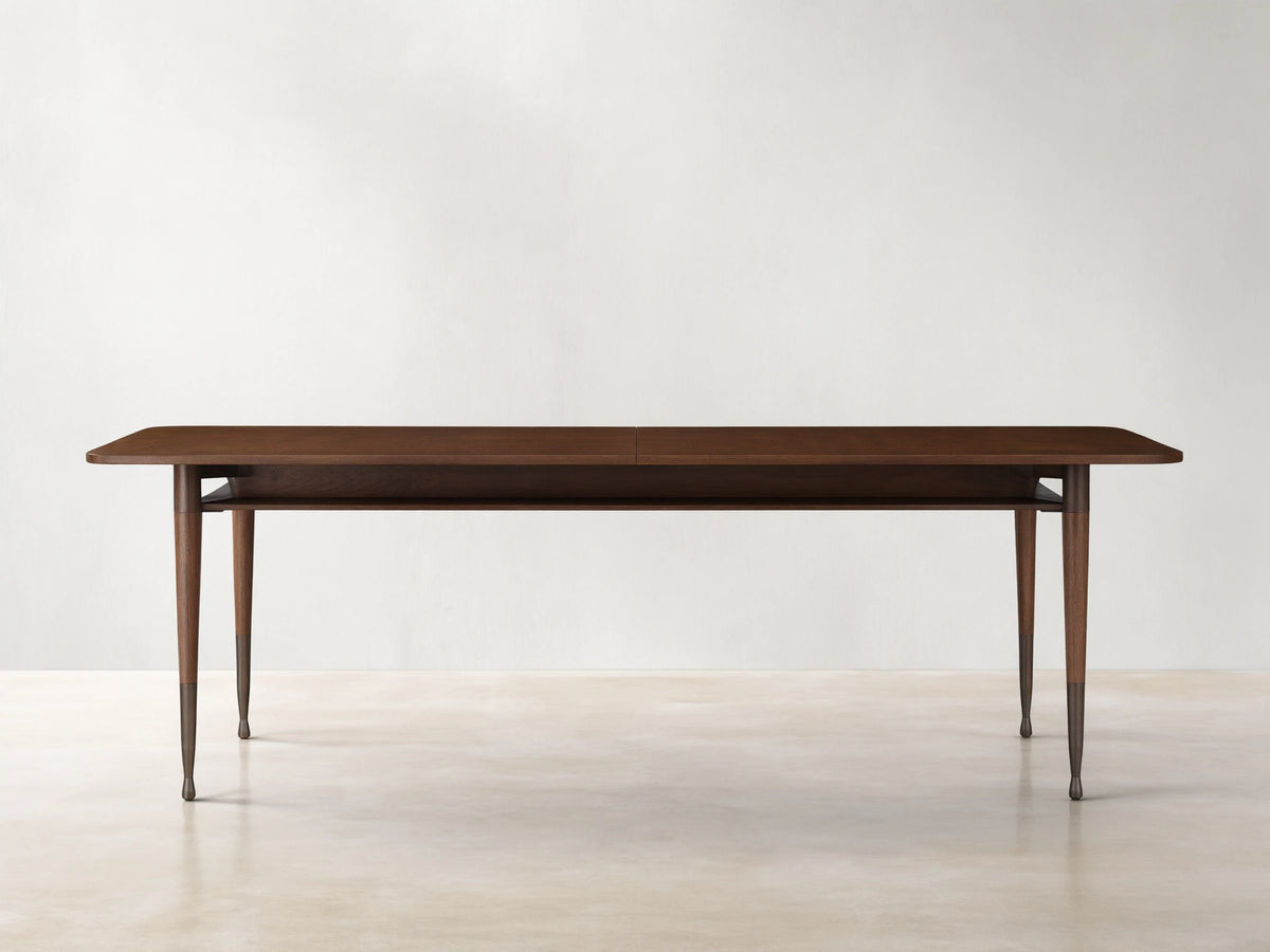 Ross Extension Dining Table made from walnut wood, featuring a long rectangular tabletop with patina brass leg caps and slender legs.