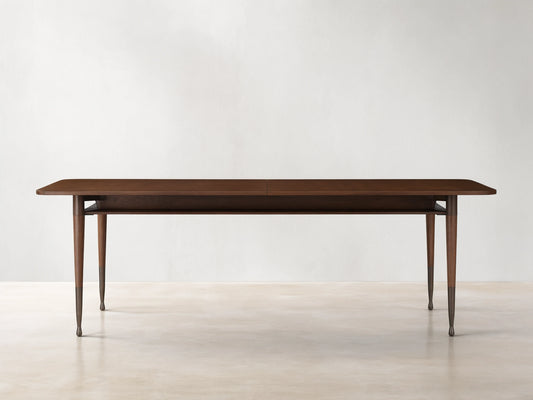 Ross Extension Dining Table made from walnut wood, featuring a long rectangular tabletop with patina brass leg caps and slender legs.