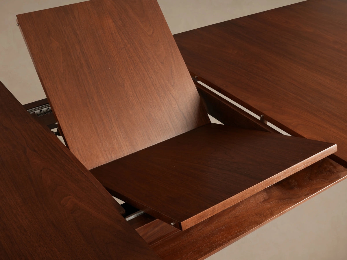 Ross Extension Dining Table in solid walnut wood, close-up of tabletop corner with floating shelf detail and patina brass leg caps.