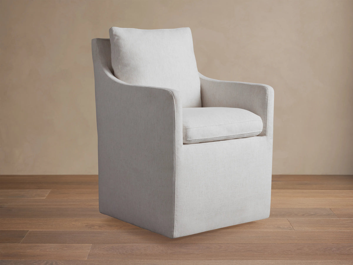 Samantha Dining Chair in light gray fabric with padded backrest and seat, featuring smooth lines and subtle curves on a wooden floor.