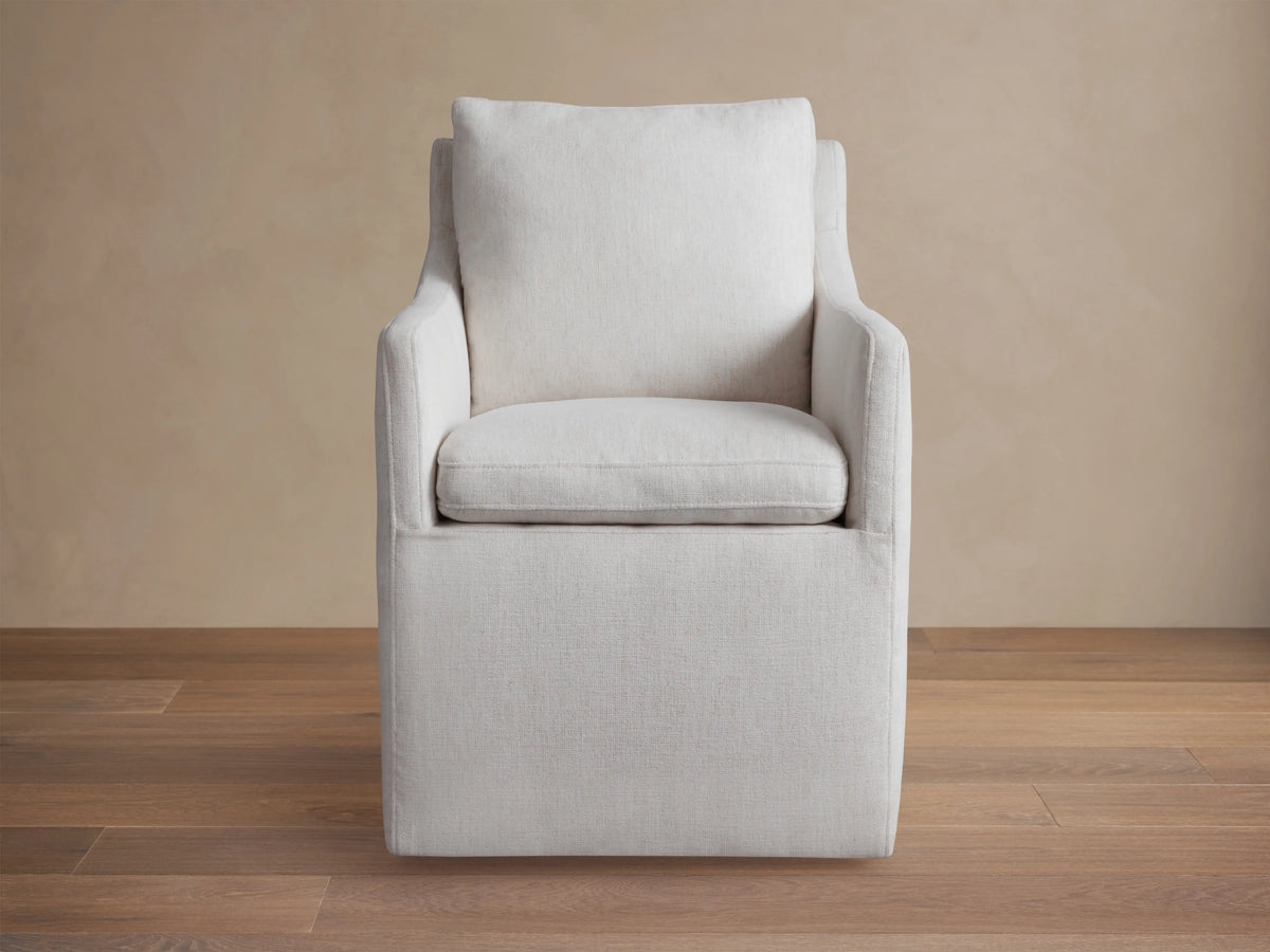 Samantha Dining Chair in light gray fabric with padded backrest and seat, featuring smooth lines and subtle curves on a wooden floor.