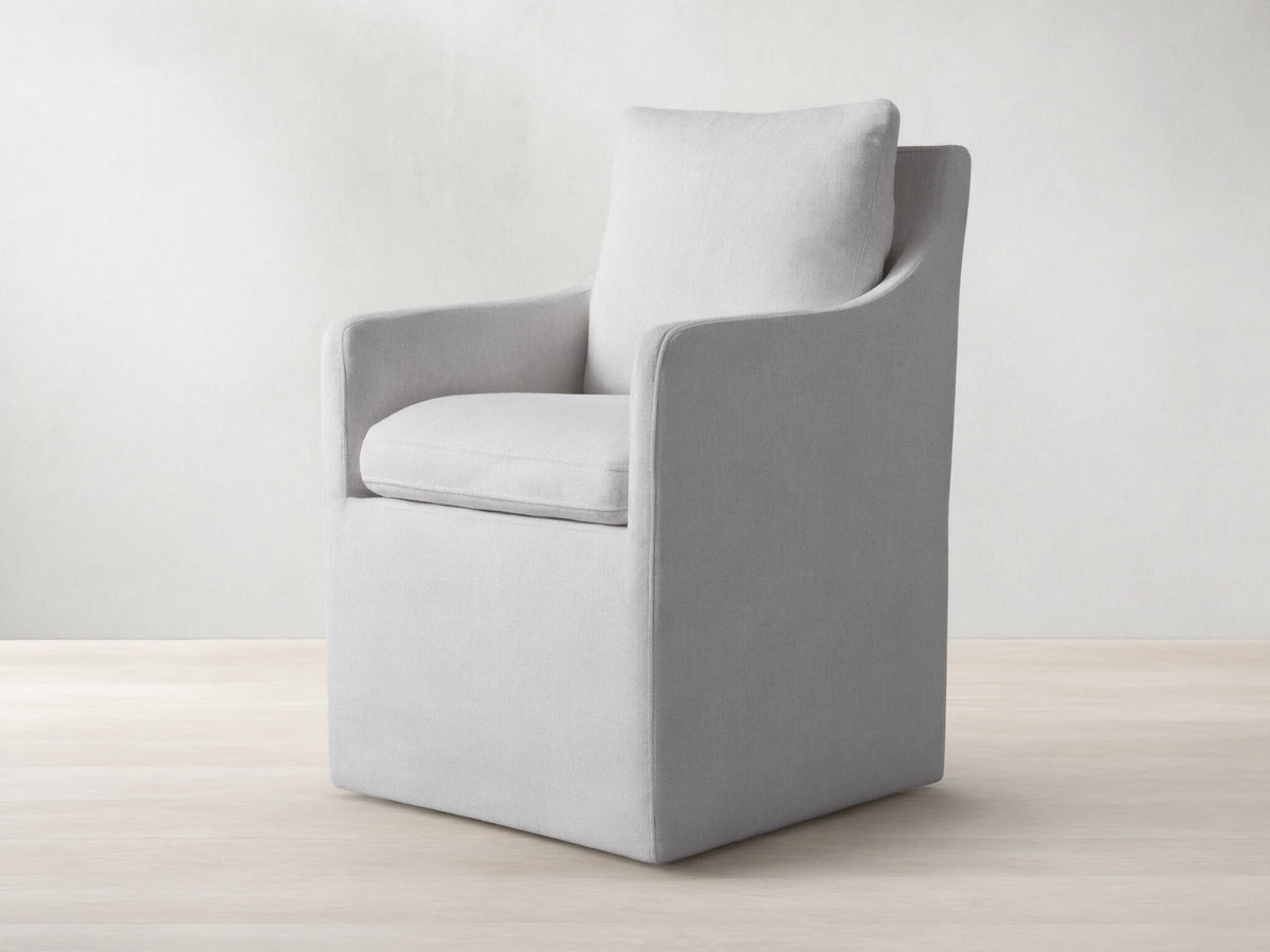 Samantha Dining Chair in light gray fabric with padded backrest and seat, featuring smooth lines and subtle curves on a wooden floor.
