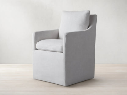 Samantha Dining Chair in light gray fabric with padded backrest and seat, featuring smooth lines and subtle curves on a wooden floor.