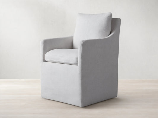 Samantha Dining Chair in light gray fabric with padded backrest and seat, featuring smooth lines and subtle curves on a wooden floor.