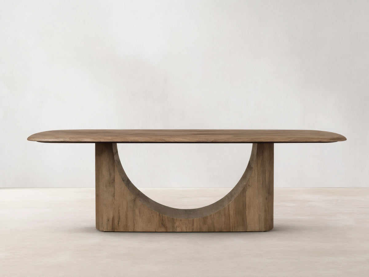 San Rafael Dining Table in primavera wood with a semi-matte finish, featuring a curved base and oval top, on hardwood floor.