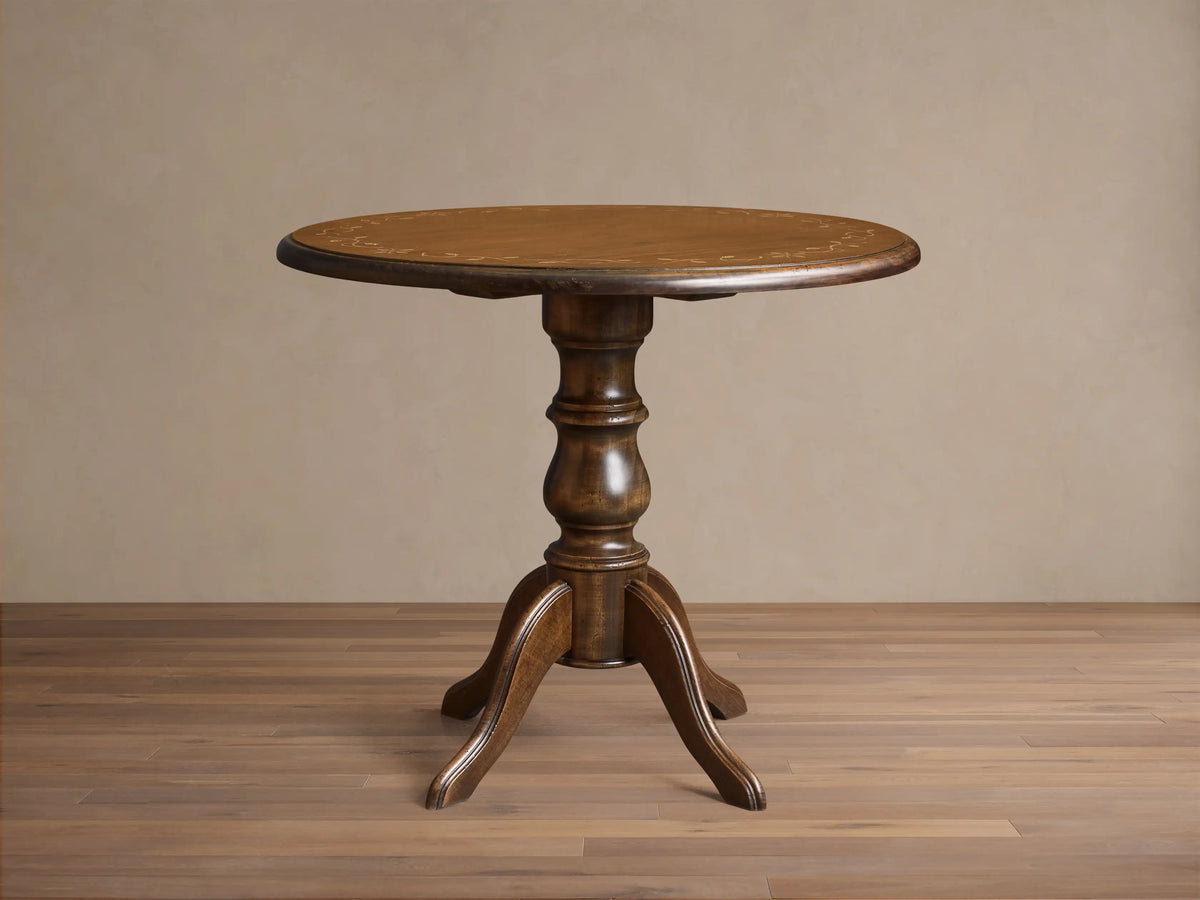 Front view of the brown Stefania Bistro Table with a round top, hand-painted botanical border, and a turned pedestal base.