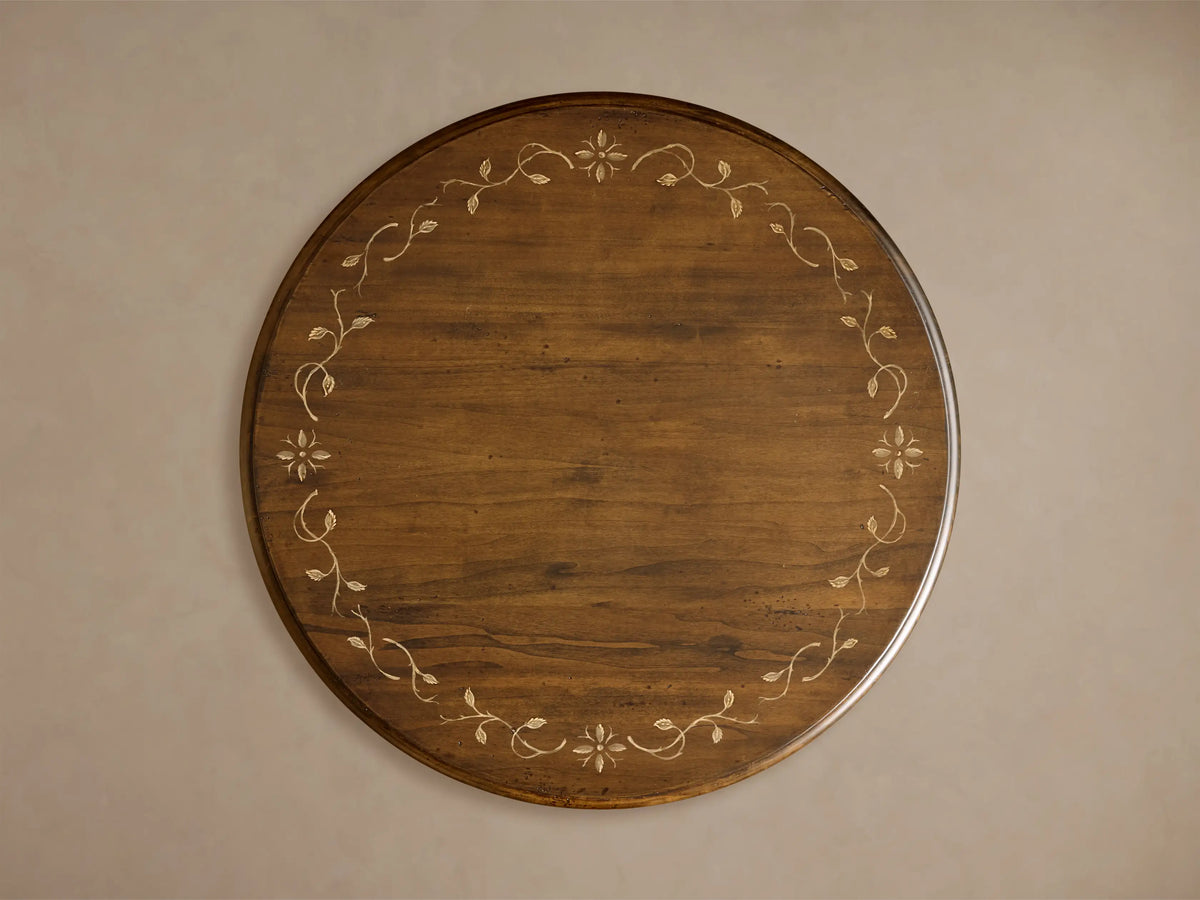 Close-up of Stefania Bistro Table, dark brown wood with a light hand-painted botanical motif on the tabletop and turned pedestal base.