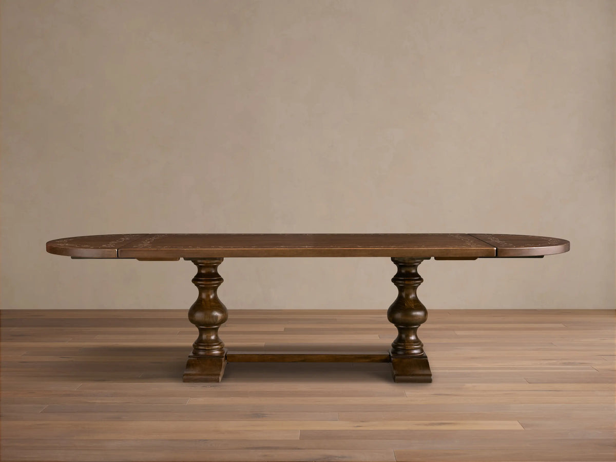 Front view of the brown Stefania Oval Extension Dining Table, with oval top featuring a botanical motif and hand-turned pedestal legs.