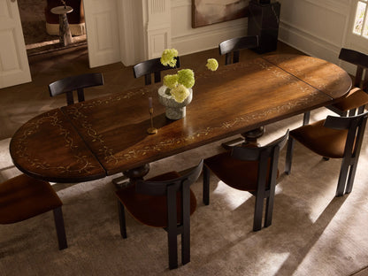 Stefania Oval Extension Dining Table, dark brown wood with hand-painted gold leafy botanical border, centered in a dining room.