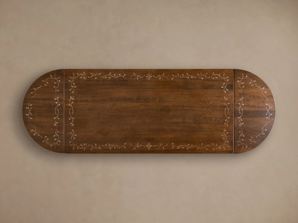 Front view of the brown Stefania Oval Extension Dining Table, with oval top featuring a botanical motif and hand-turned pedestal legs.