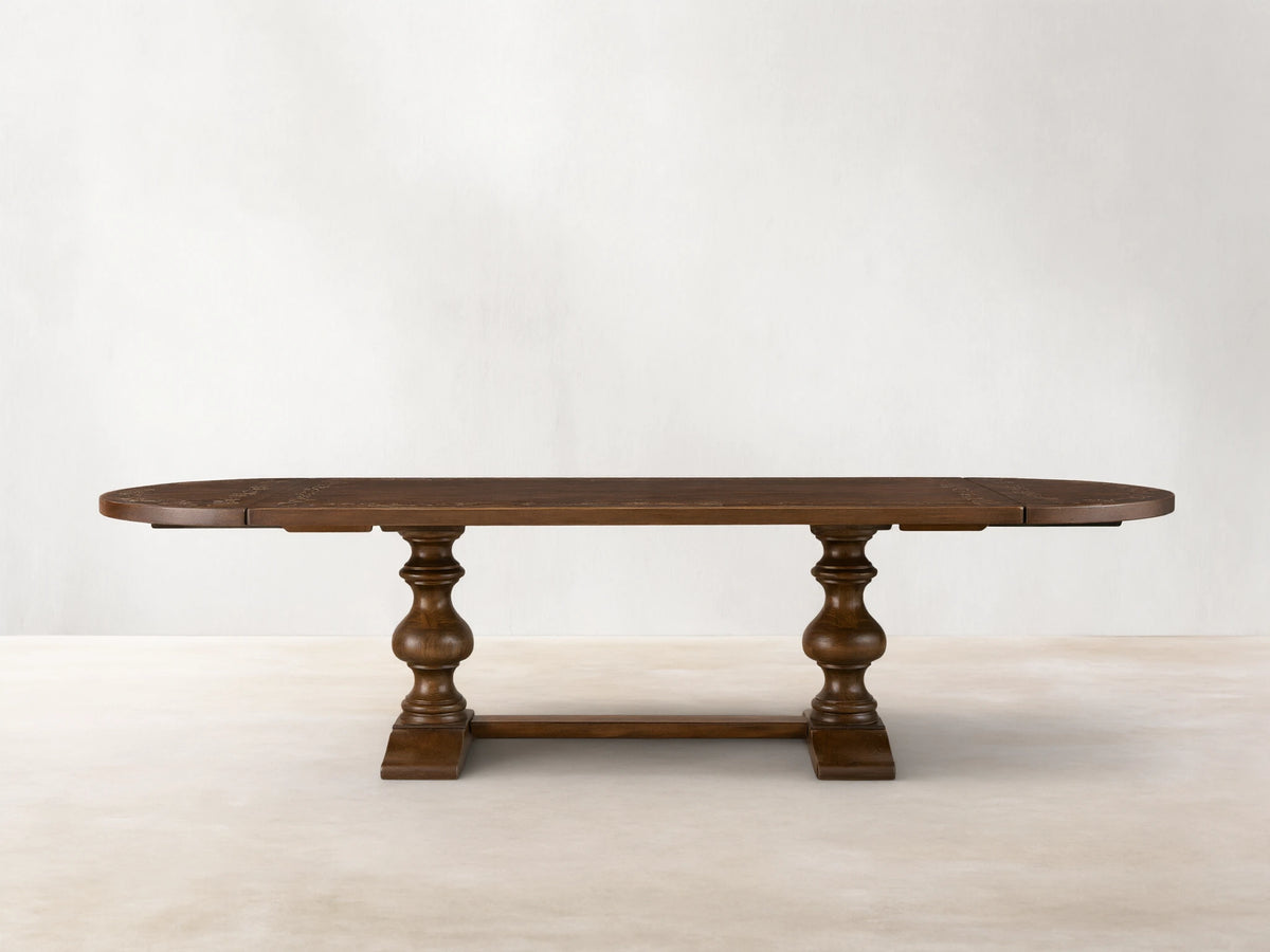 Front view of the brown Stefania Oval Extension Dining Table, with oval top featuring a botanical motif and hand-turned pedestal legs.