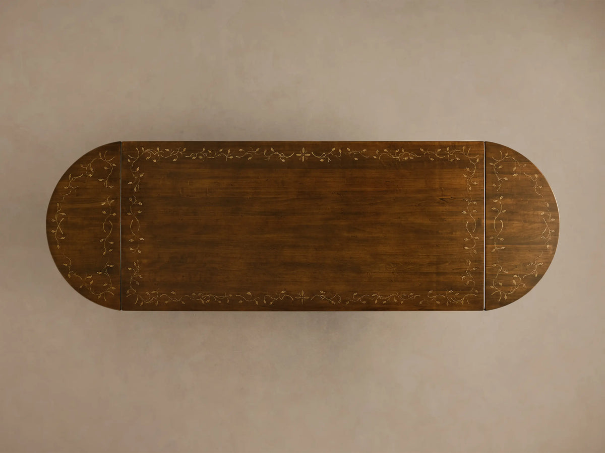 Close-up angled view of the dark brown Stefania Oval Extension Dining Table, showing the hand-painted leafy botanical motif on the tabletop and part of the hand-turned pedestal leg.