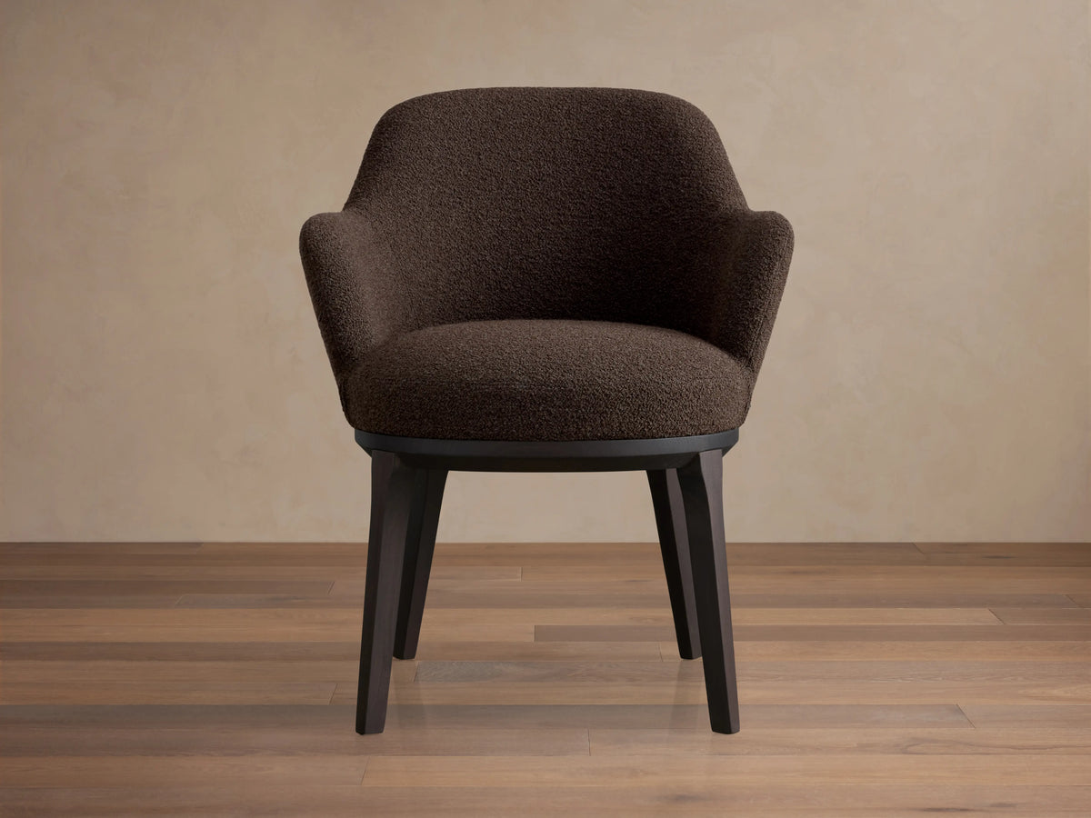 Simone Dining Arm Chair with a textured brown upholstered seat and backrest, featuring curved armrests on dark wooden legs, on a wooden floor.