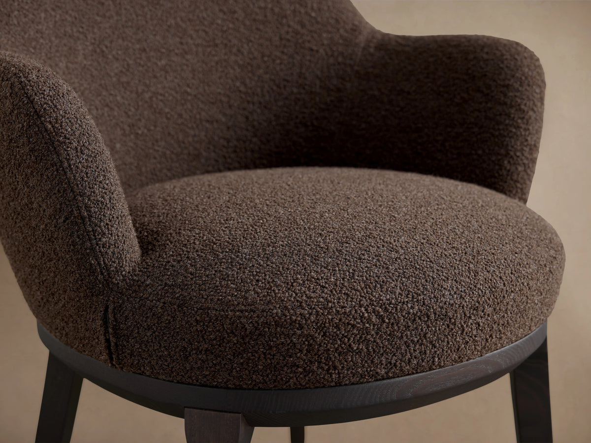 Simone Dining Arm Chair in dark brown fabric, featuring a rounded backrest and armrests, with a solid dark ash wood frame.
