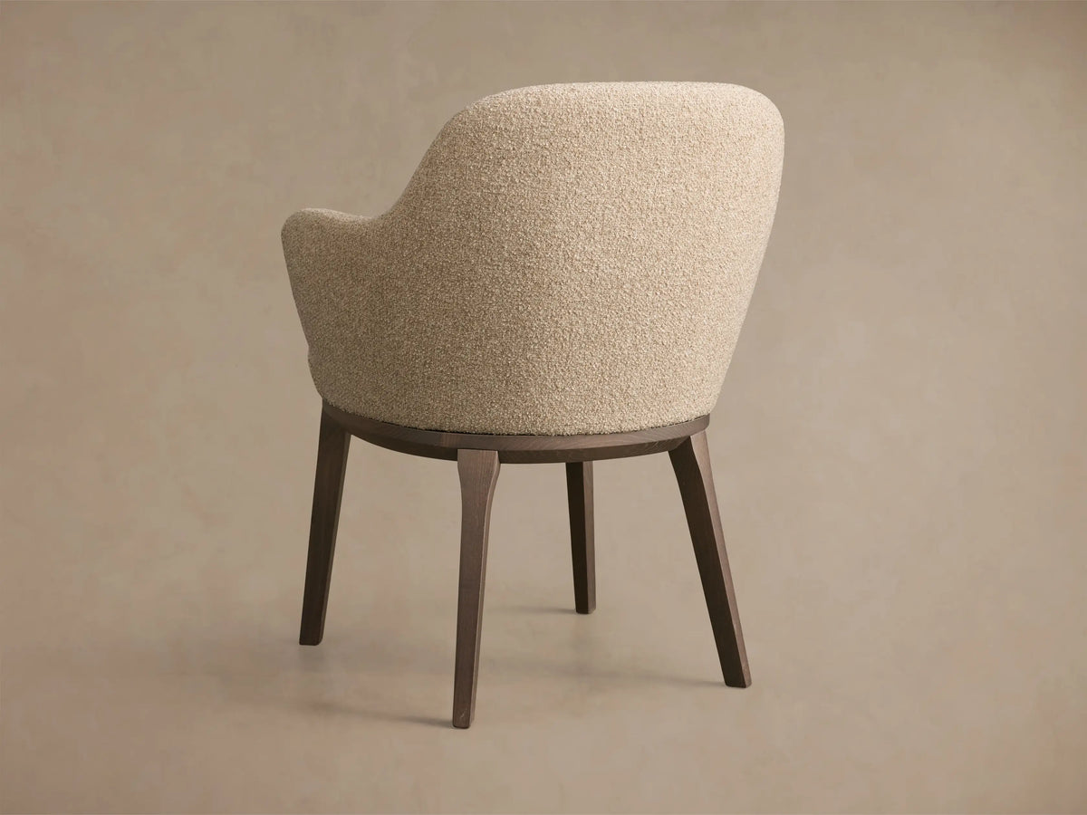 Close-up of the textured beige upholstered Simone Dining Arm Chair, with curved arms and dark brown wood frame.