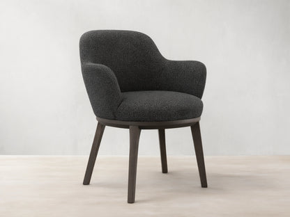 Front view of the dark gray tweed Simone Dining Arm Chair with dark wood legs and a rounded back.