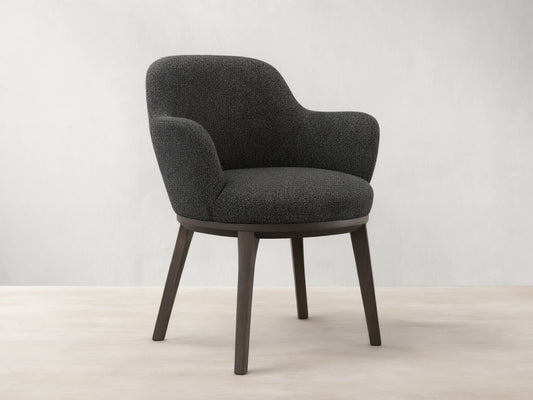 Front view of the dark gray tweed Simone Dining Arm Chair with dark wood legs and a rounded back.