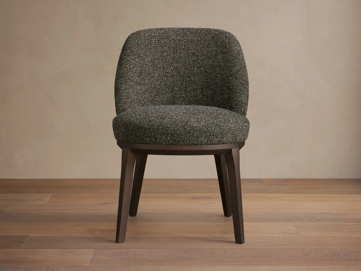 Front view of a dark speckled upholstered Simone Dining Side Chair with dark wood legs and a curved back.