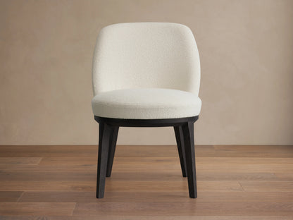 Simone Dining Side Chair with a plush, cream upholstered seat and backrest, set on four black solid ash wood legs on a wooden floor.