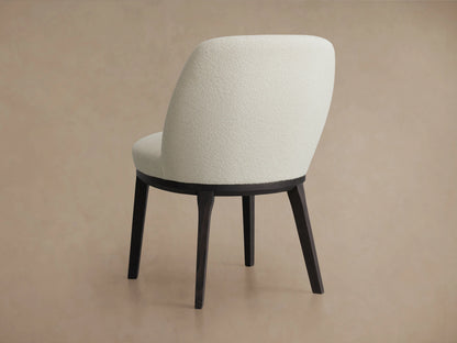 Simone Dining Side Chair with a textured cream upholstered seat and curved backrest. The base is dark wood, showcasing elegant craftsmanship.