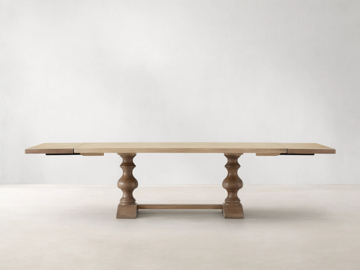 Tuscany Extension Dining Table with a light wood finish, two pedestal legs, and extended leaves on both ends against a neutral background.