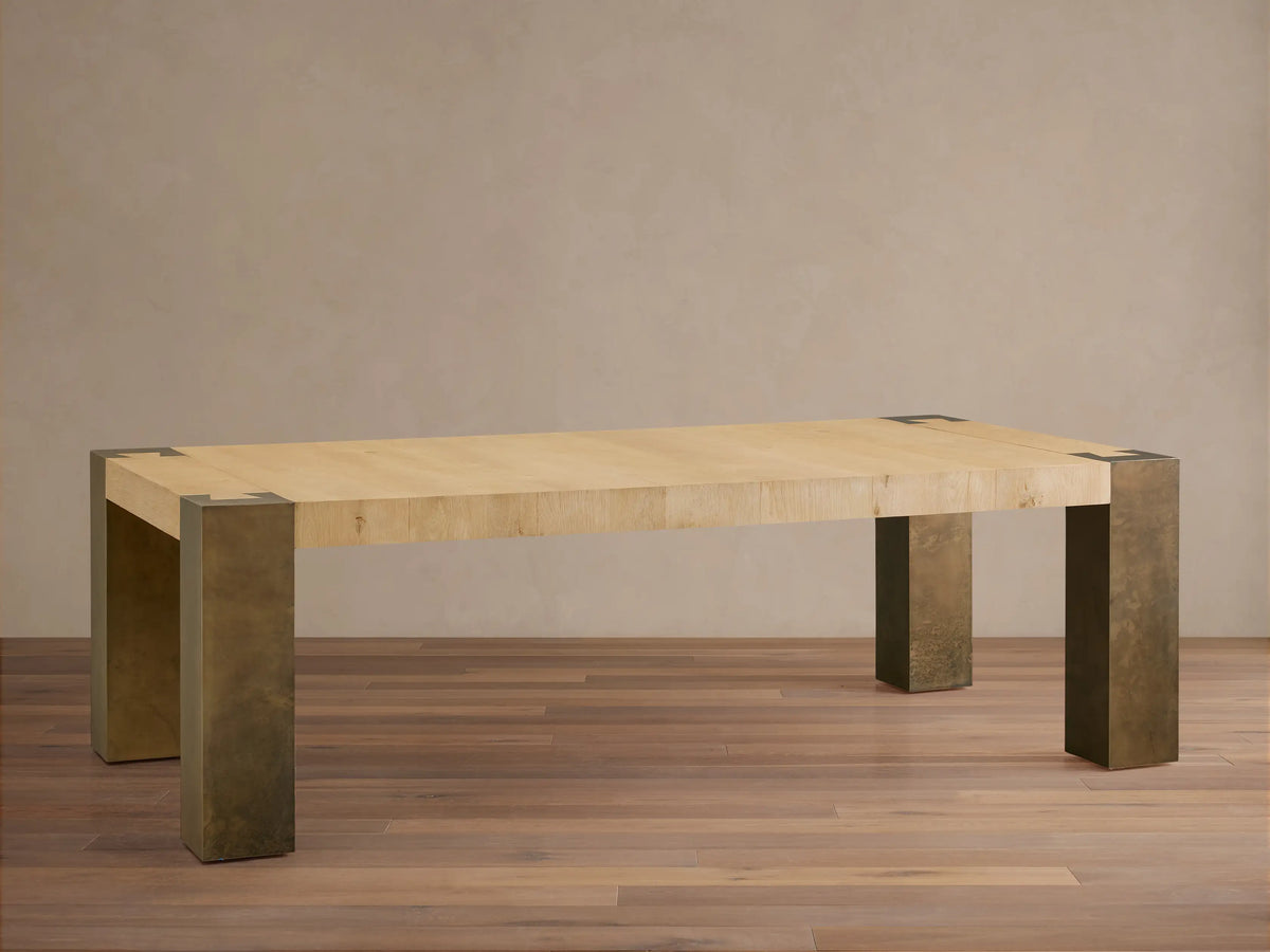 Telluride Dining Table with light wood top, dark oxidized steel legs, and corner accents, angled on a wood floor.