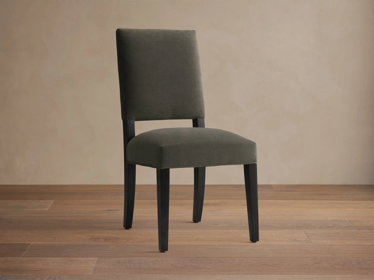 Torino Dining Chair with dark fabric upholstery, solid tapered maple legs on wooden floor, against a neutral wall.