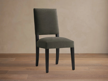 Torino Dining Chair with dark fabric upholstery, solid tapered maple legs on wooden floor, against a neutral wall.