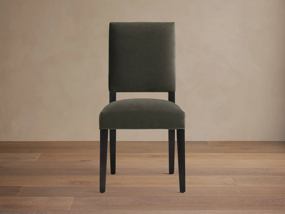 Torino Dining Chair with dark fabric upholstery, solid tapered maple legs on wooden floor, against a neutral wall.