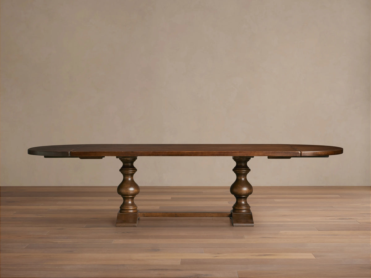 Tuscany Oval Extension Dining Table in dark wood, with an oval shape and hand-turned pedestal legs on a wooden floor.