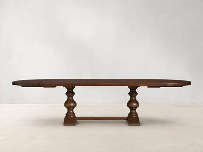 Tuscany Oval Extension Dining Table in dark wood, with an oval shape and hand-turned pedestal legs on a wooden floor.