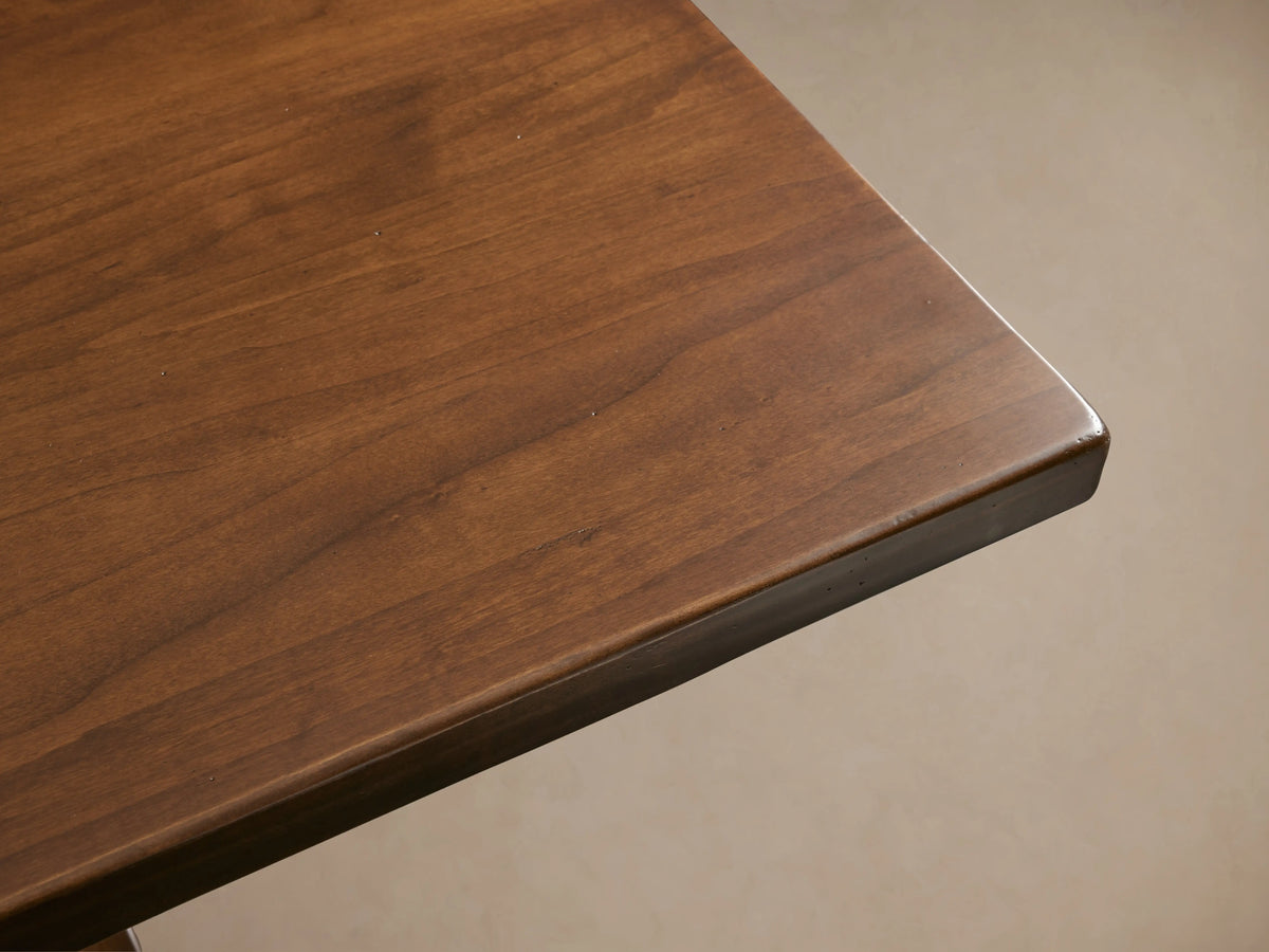Tuscany Extension Dining Table with a rich brown finish, hand-turned pedestal legs, and horizontal trestle, sits in a room.
