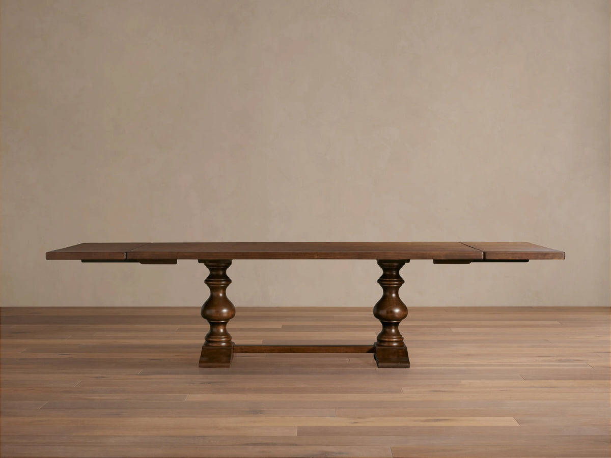 Tuscany Extension Dining Table in warm brown poplar wood, features hand-turned pedestal legs, horizontal trestle, and antiqued finish.