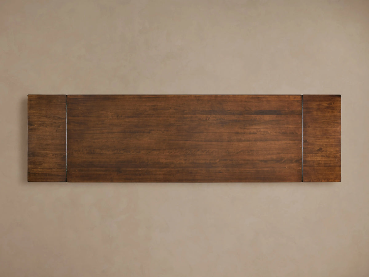 Tuscany Extension Dining Table in dark brown poplar wood, featuring hand-turned pedestal legs and a horizontal trestle on a wooden floor.