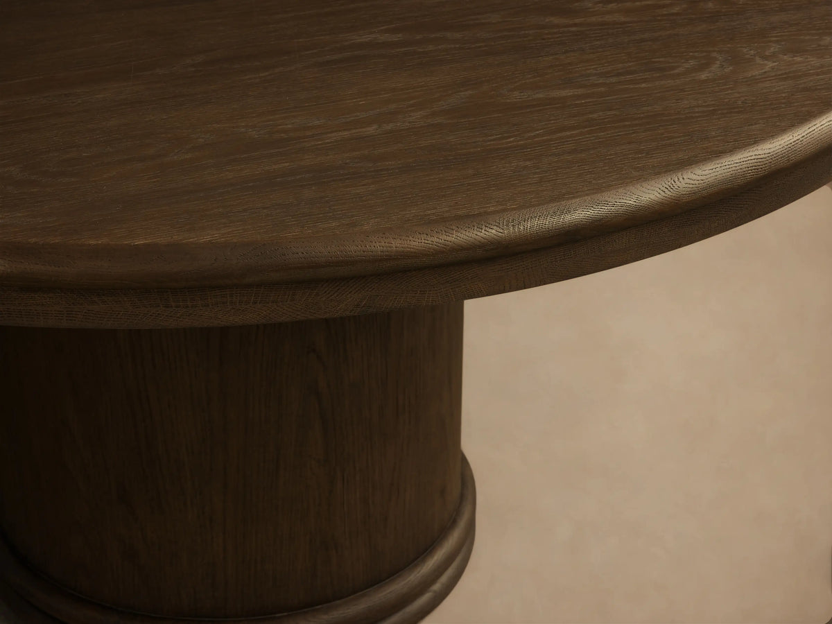 Front view of a mocha-toned Warby Round Dining Table, featuring a smooth round top and a thick cylindrical pedestal base.