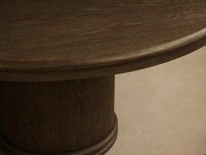 Front view of a mocha-toned Warby Round Dining Table, featuring a smooth round top and a thick cylindrical pedestal base.