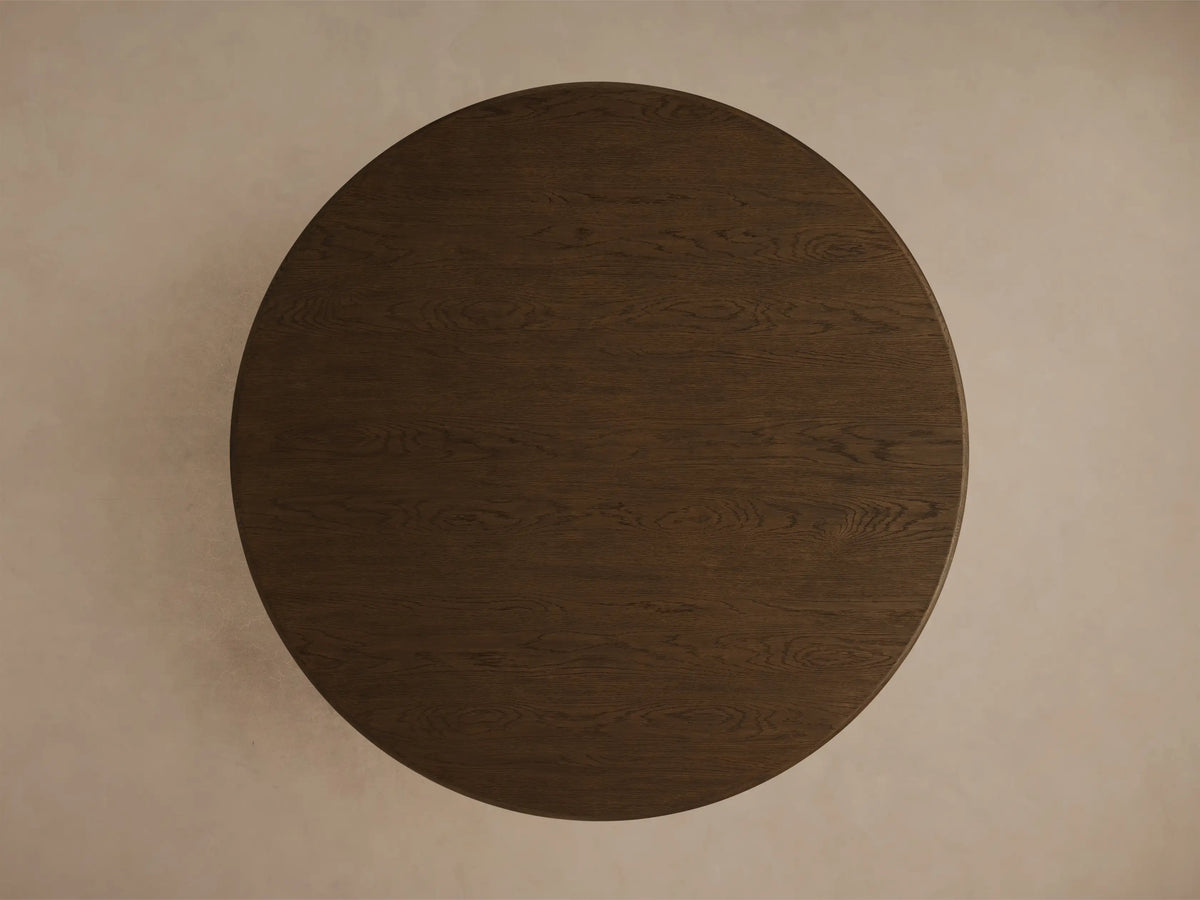 Close-up of the mocha-toned Warby Round Dining Table, showing the smooth, rounded edge of the tabletop and the pedestal base.