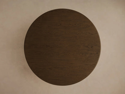 Close-up of the mocha-toned Warby Round Dining Table, showing the smooth, rounded edge of the tabletop and the pedestal base.