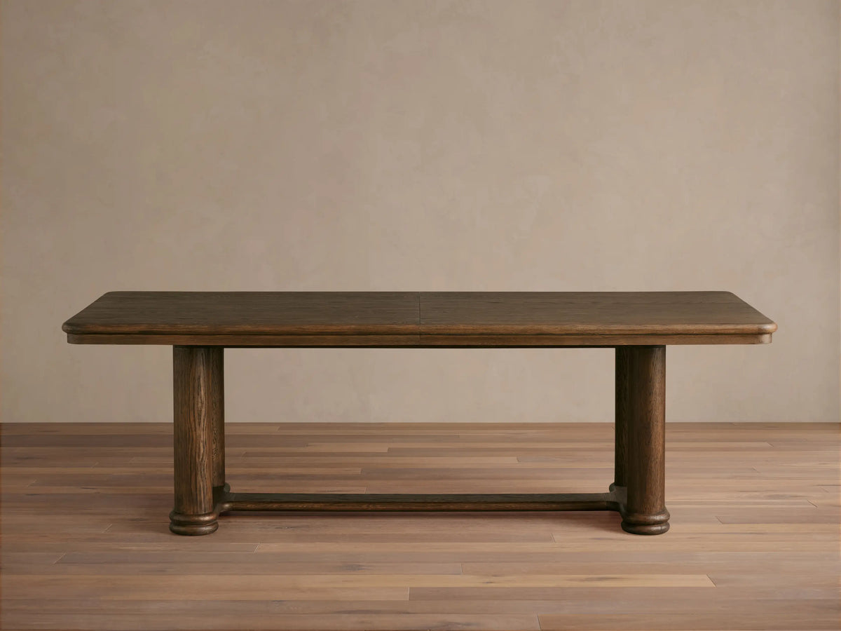 Warby Extension Dining Table in dark wood finish, featuring a rectangular top and two cylindrical pedestal legs on a wooden floor.