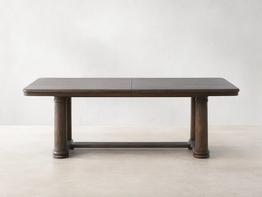 Warby Extension Dining Table in dark wood finish, featuring a rectangular top and two cylindrical pedestal legs on a wooden floor.