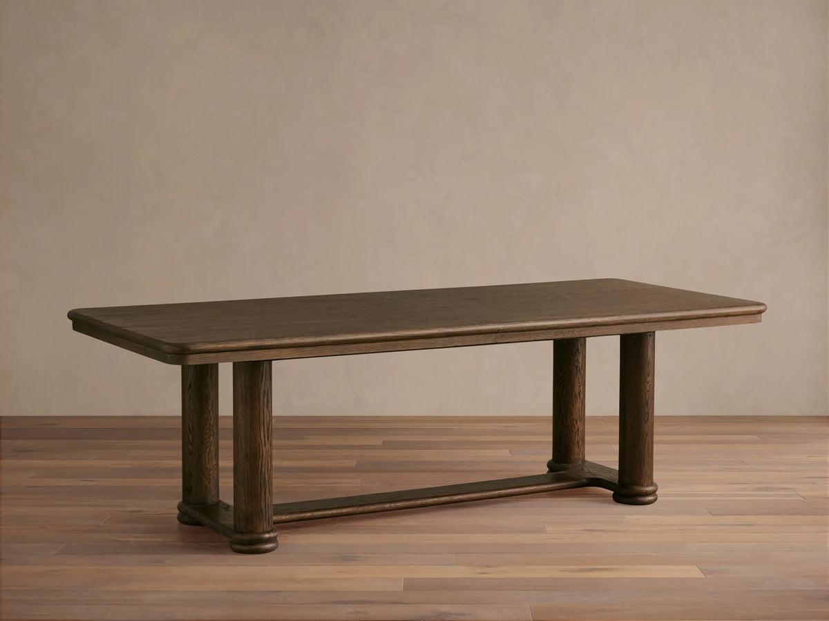 Warby Extension Dining Table in dark wood finish, rectangular shape with two cylindrical legs, on light wooden floor.