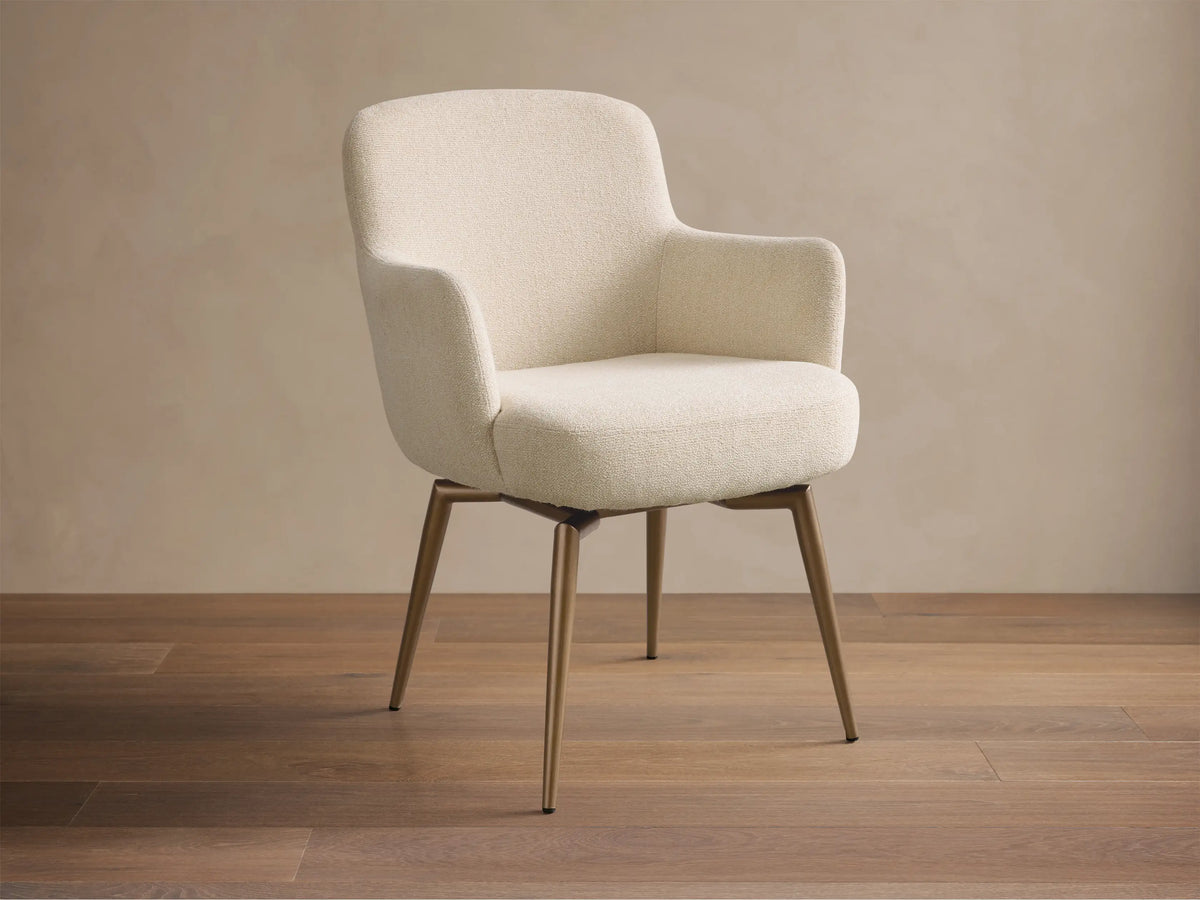 Front view of the cream upholstered Willem Dining Arm Chair with curved back, armrests, and antique brass finish metal legs.